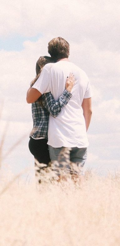 Ein Paar umarmt sich von hinten in einer landschaftlichen Umgebung.