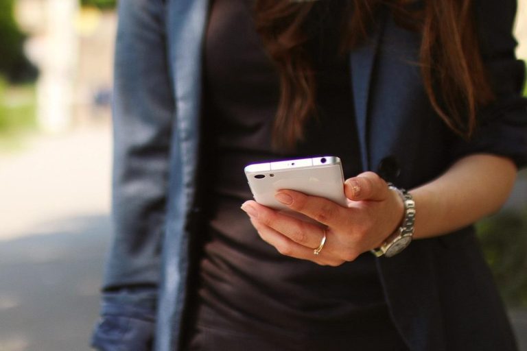 Eine Person hält ein Smartphone in der Hand, steht auf einem Gehweg.