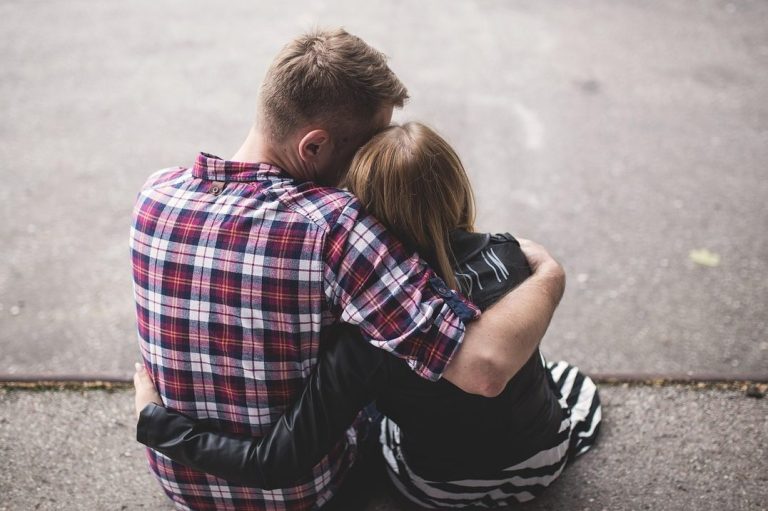 Junge und Mädchen sitzen eng umarmt und schauen nach vorne.