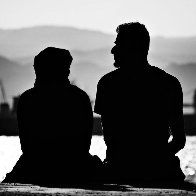 Silhouetten von zwei Personen, die am Ufer sitzen und auf das Wasser blicken. Bindungsangst verstehen.